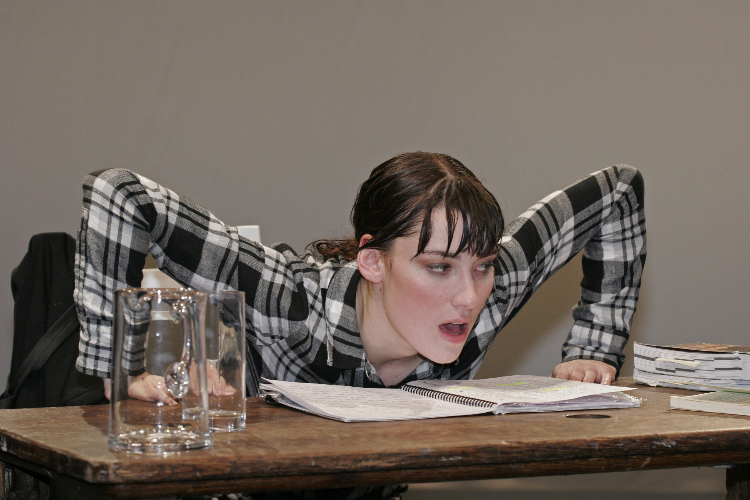 Performer in a plaid shirt leaning over a notebook at a wooden table