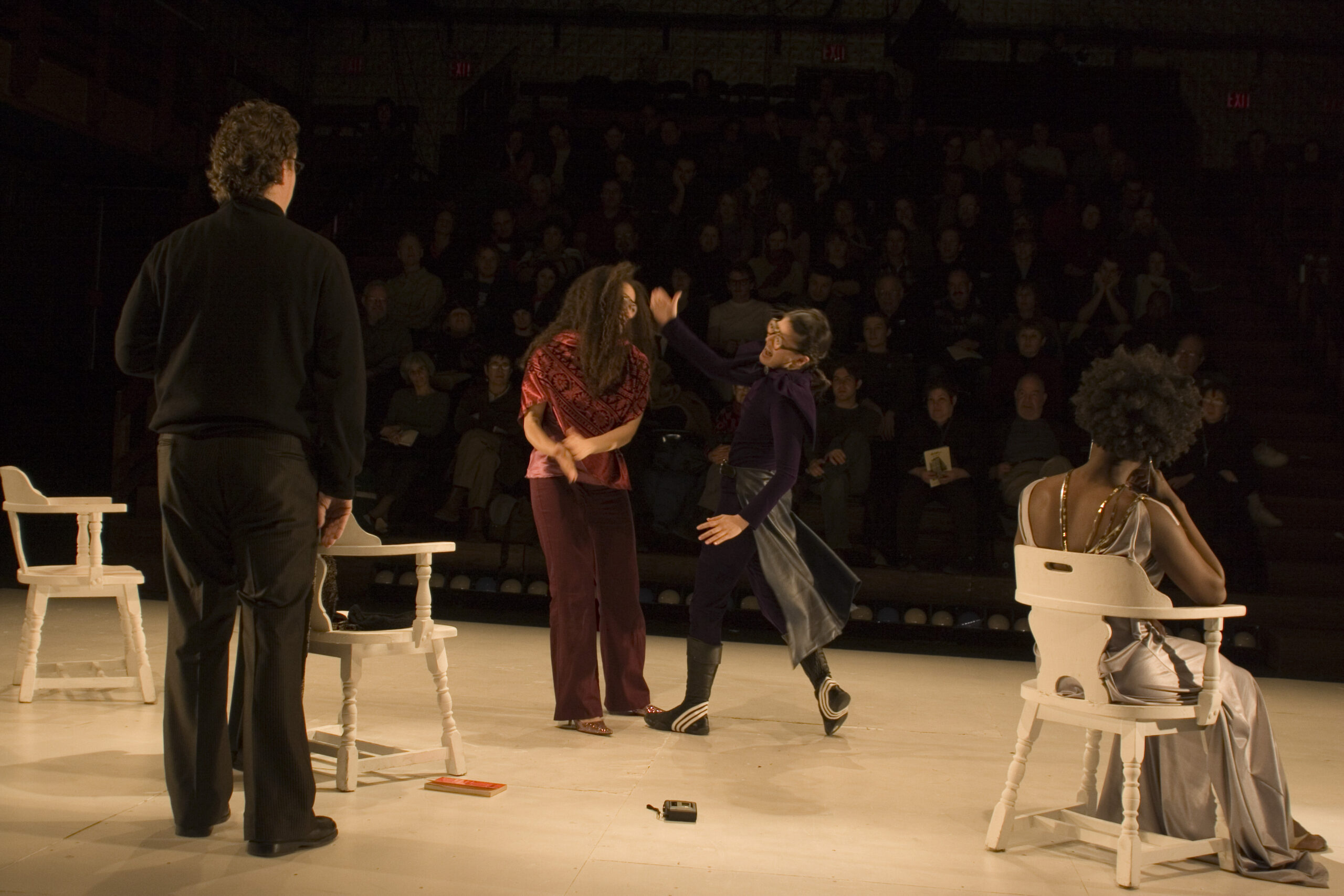 Three performers on stage with white chairs during a Schechner production